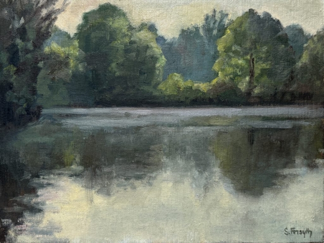 Morning colours and mist hover over the water. Backlit trees reflect in the water.